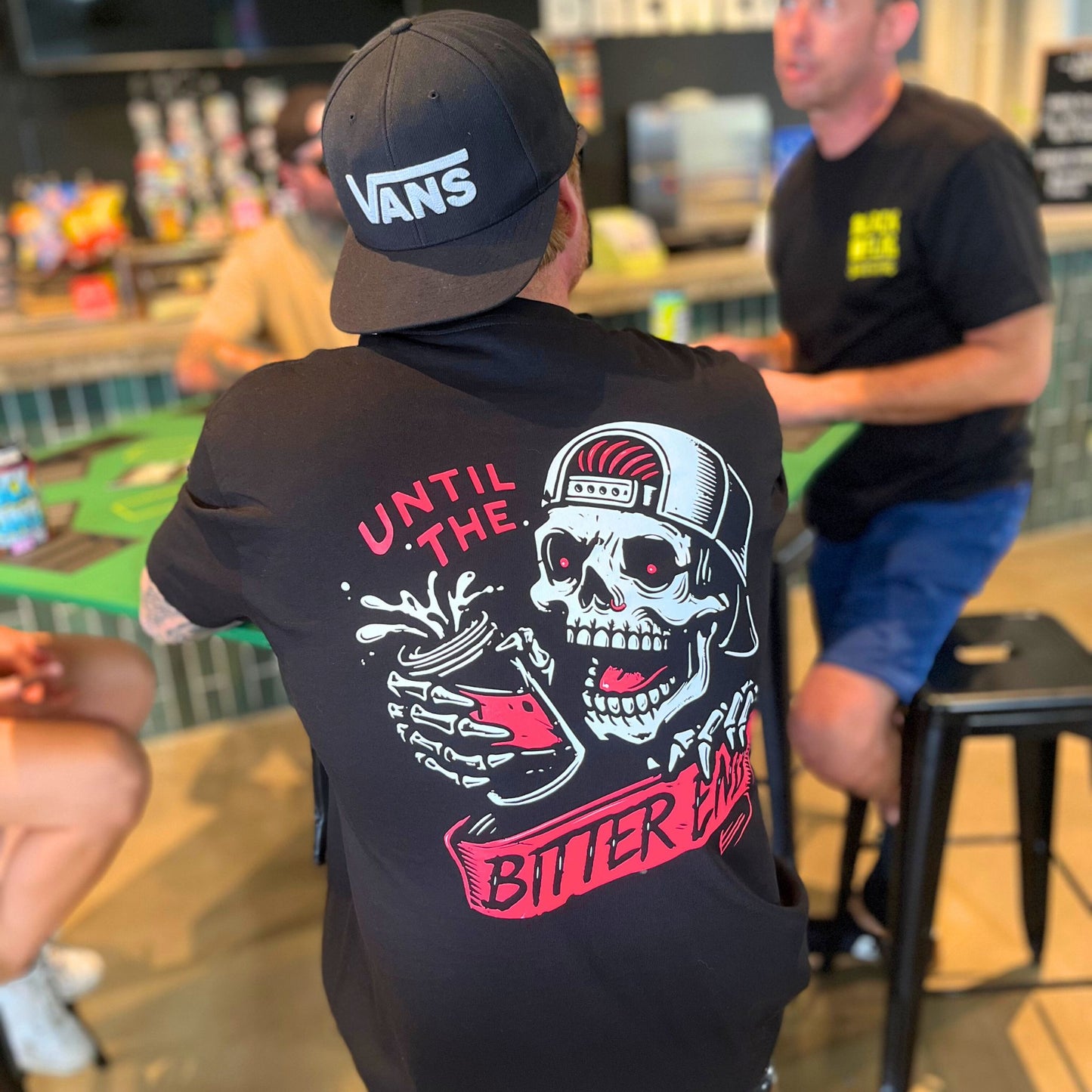 Man wearing a black Blackflag t-shirt with hand drawn Until The Bitter End illustration on back.